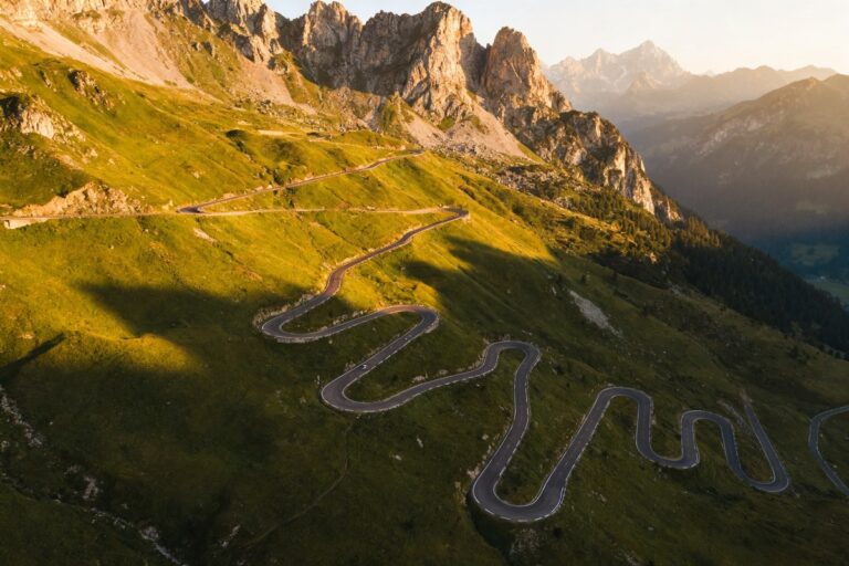 Route de montagne aux nombreux lacets grimpant un versant alpin verdoyant sous la lumière d'été