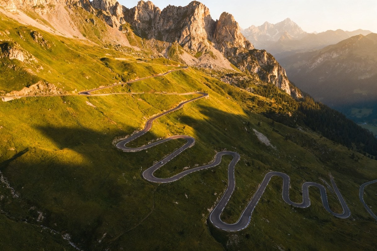 Route de montagne aux nombreux lacets grimpant un versant alpin verdoyant sous la lumière d'été