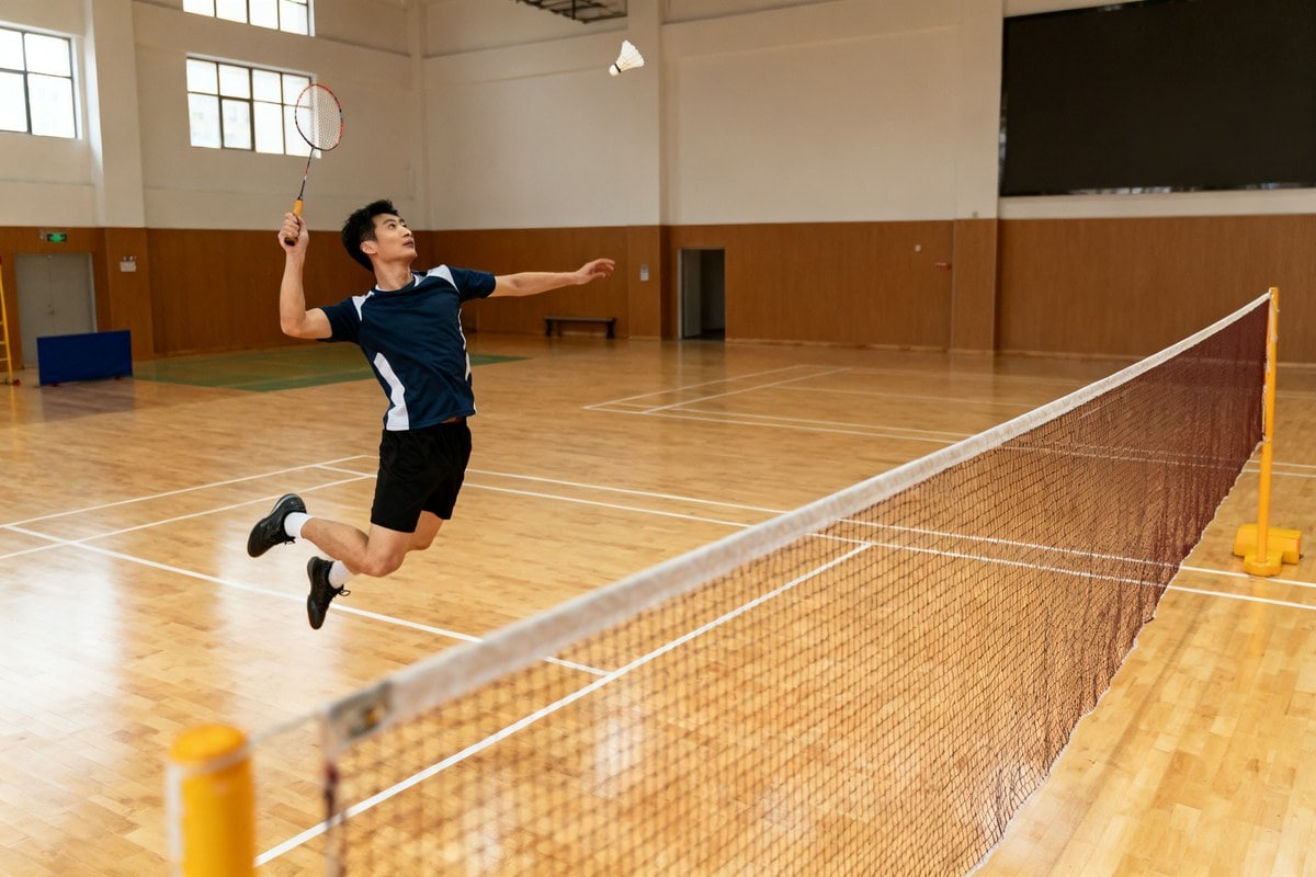 Joueur de badminton bondissant pour smasher un volant dans un gymnase lumineux