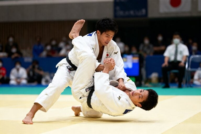 Deux judokas en kimono blanc exécutent une projection sur un tatami, ceinture noire, lors d'un combat