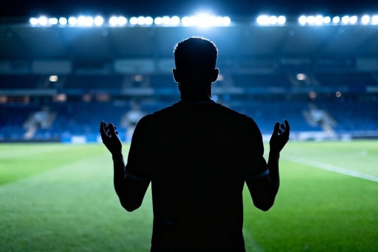 Silhouette d'un footballeur vue de dos sur une pelouse de stade illuminée la nuit