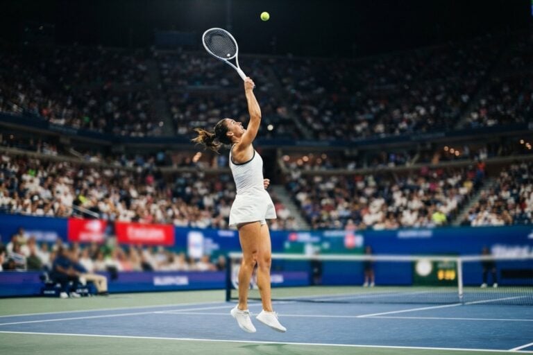 Joueuse de tennis au service sur un court en dur bleu, devant un stade plein en nocturne