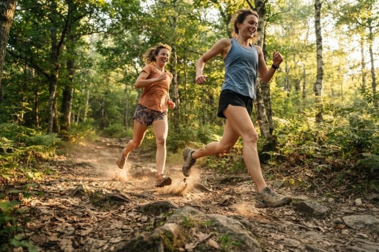 Deux coureuses en foulée sur un sentier forestier caillouteux, chaussures de trail soulevant la poussière