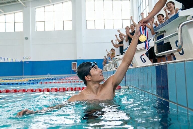 Un nageur dans le bassin tend sa médaille d'or vers des spectateurs penchés au bord de la piscine