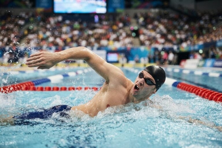 Un nageur en plein crawl dans une piscine olympique, bras hors de l'eau, devant des tribunes pleines