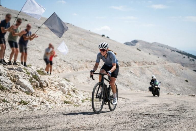 Une cycliste seule en pleine ascension sur une route de montagne calcaire, encouragée par des spectateurs