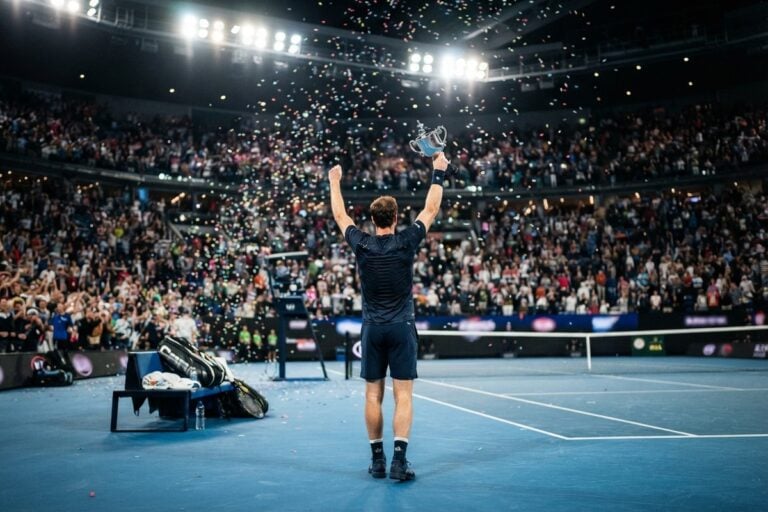 Un joueur de tennis vu de dos brandit un trophée au centre d'un court bleu sous les confettis