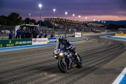 Un pilote d'endurance moto sort d'un virage au crépuscule, devant les stands et une tribune pleine