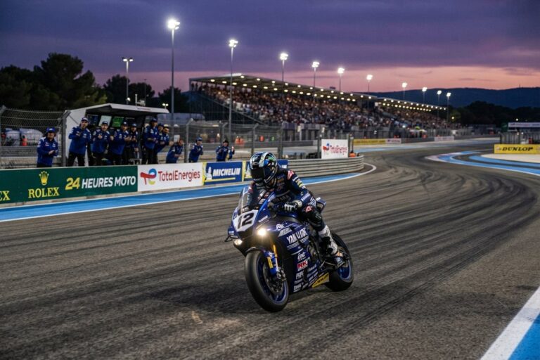 Un pilote d'endurance moto sort d'un virage au crépuscule, devant les stands et une tribune pleine