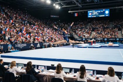 Une gymnaste de l'équipe de France réalise un saut en grand écart sur le praticable, devant les juges et des tribunes pleines