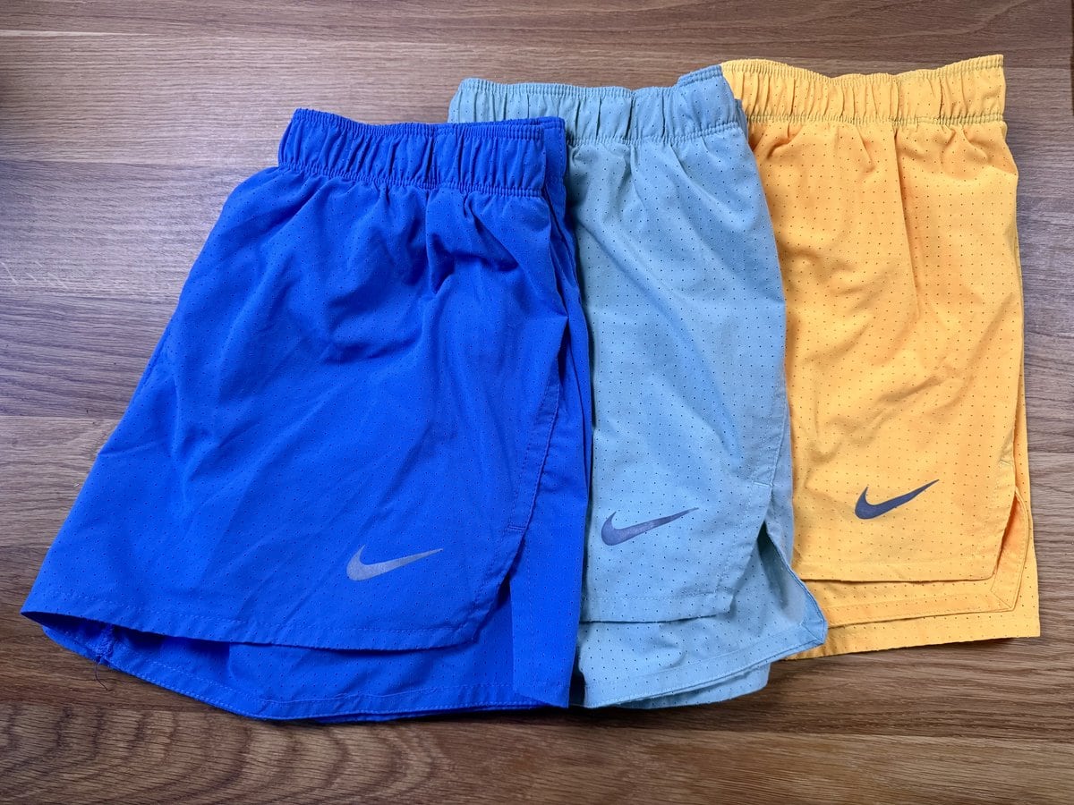 Trois shorts de running Nike Fast bleu, vert d'eau et orange posés à plat sur un parquet