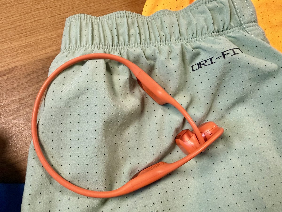 Gros plan sur la ceinture Dri-FIT d'un short vert d'eau, avec un casque à conduction osseuse orange posé dessus