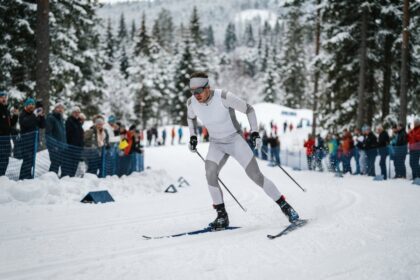 Un skieur de fond en combinaison blanche sans marquage s'élance sur une piste damée devant des spectateurs