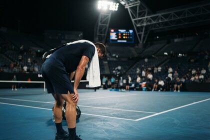 Un joueur de tennis épuisé, mains sur les genoux et serviette sur l'épaule, sur un court en dur éclairé la nuit