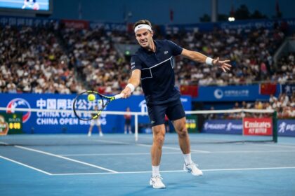 Un joueur de tennis au bandeau blanc frappe un revers sur un court bleu, devant les tribunes pleines de l'Open de Chine