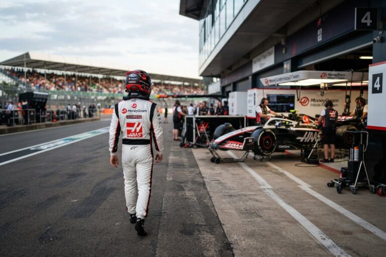 Pilote casqué en combinaison Haas marchant de dos dans la voie des stands vers le garage de l'écurie