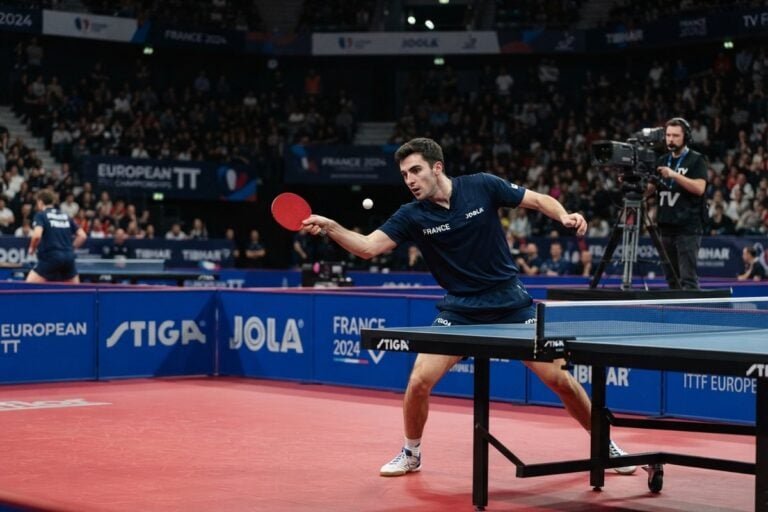 Pongiste en maillot bleu de l'équipe de France frappant un coup droit lors d'un match dans une salle comble