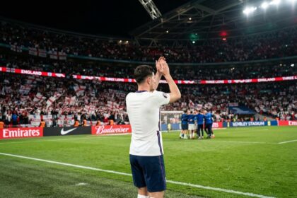 Joueur anglais de dos applaudissant les supporters dans un stade de Wembley plein, drapeaux de Saint-Georges en tribunes