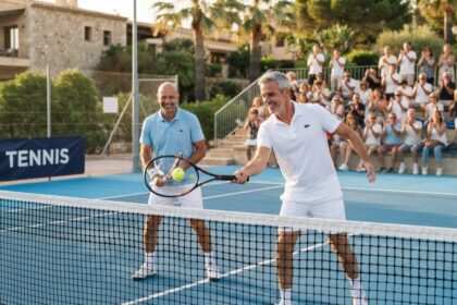 Deux joueurs de tennis d'une cinquantaine d'années au filet lors d'un double, devant des spectateurs qui applaudissent