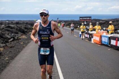 Triathlète en tenue de l'équipe de France courant sur une route bordée de lave, ravitaillement en arrière-plan