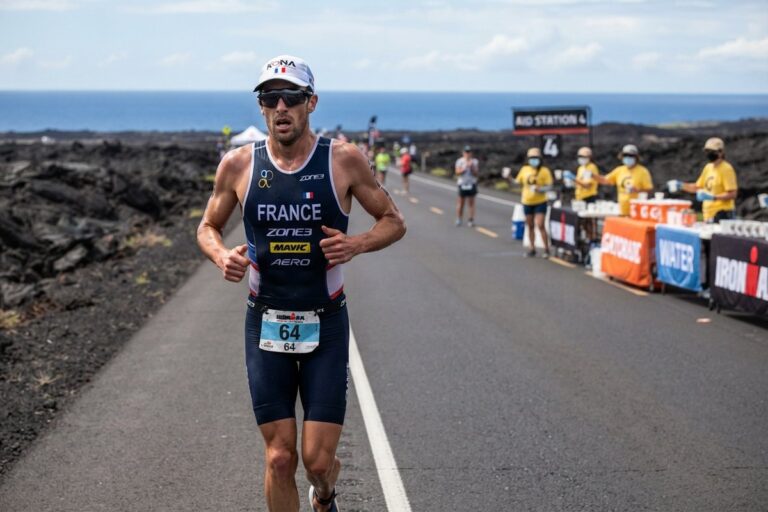 Triathlète en tenue de l'équipe de France courant sur une route bordée de lave, ravitaillement en arrière-plan